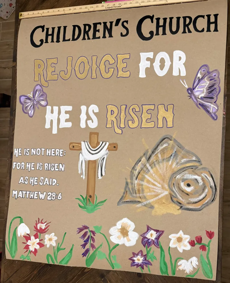 Tall hand-painted Easter banner for children's church reading Rejoice for He Is Risen with a cross, the empty tomb, butterflies and spring flowers