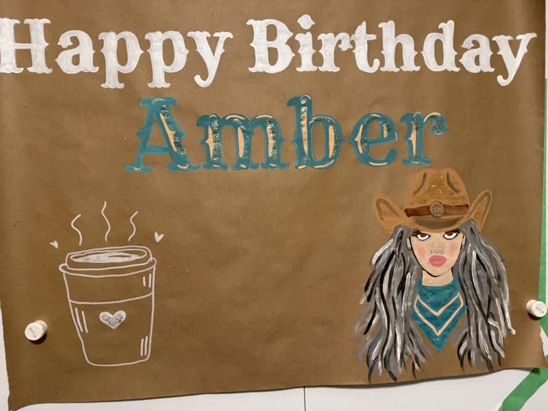 Hand-painted birthday banner reading Happy Birthday Amber with a painted cowgirl portrait and a coffee cup