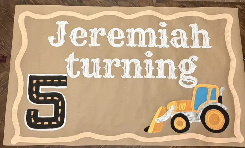 Hand-painted construction-themed fifth birthday banner reading Jeremiah turning 5 with a road-marking number five and a yellow tractor