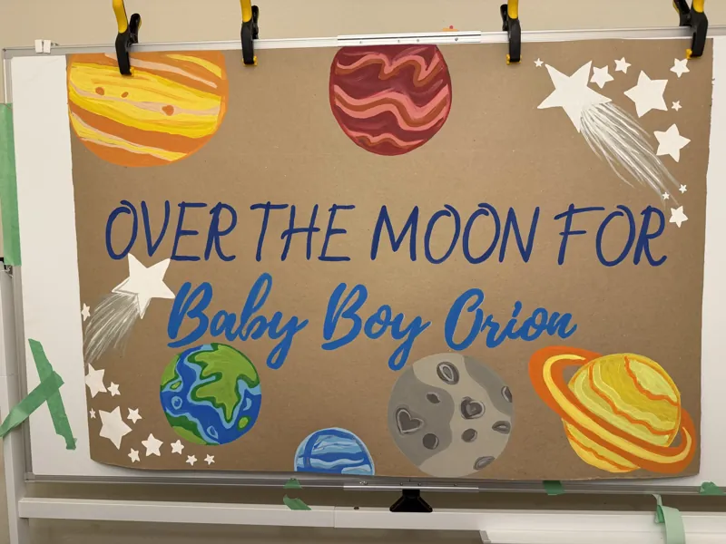 Hand-painted baby shower banner reading Over the Moon for Baby Boy Orion surrounded by planets, stars and shooting stars